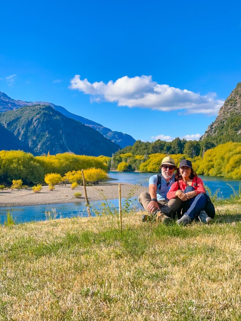 Dos personas sentadas frente a un lago sonriendo